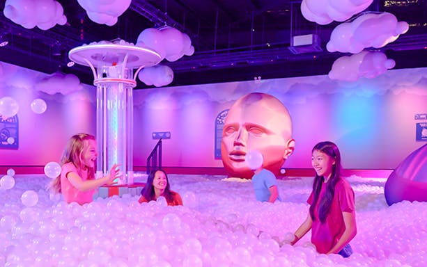Visitors enjoying bubble room at Bubble Planet An Experience Museum with large head sculpture.