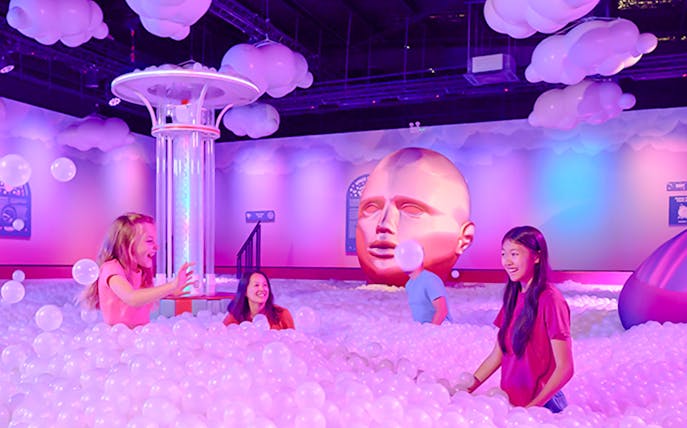 Visitors enjoying bubble room at Bubble Planet An Experience Museum with large head sculpture.