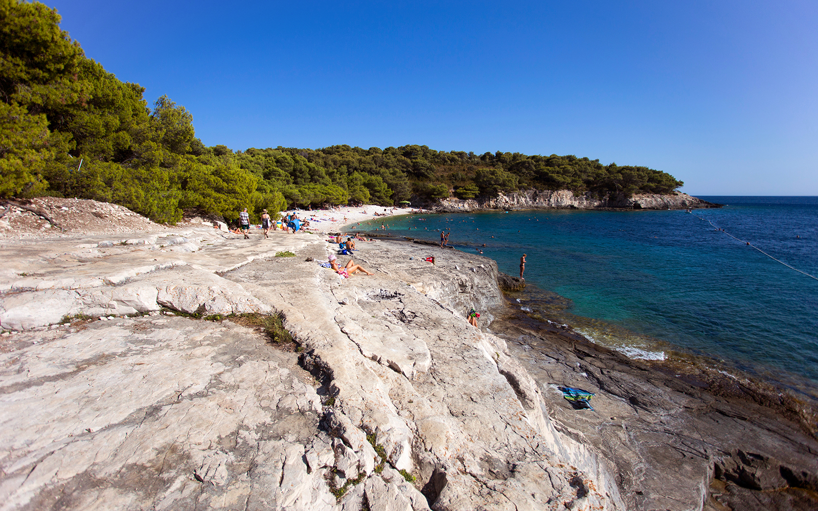 People relaxing on rocky shore at Srebrena beach, Vis island, Croatia.