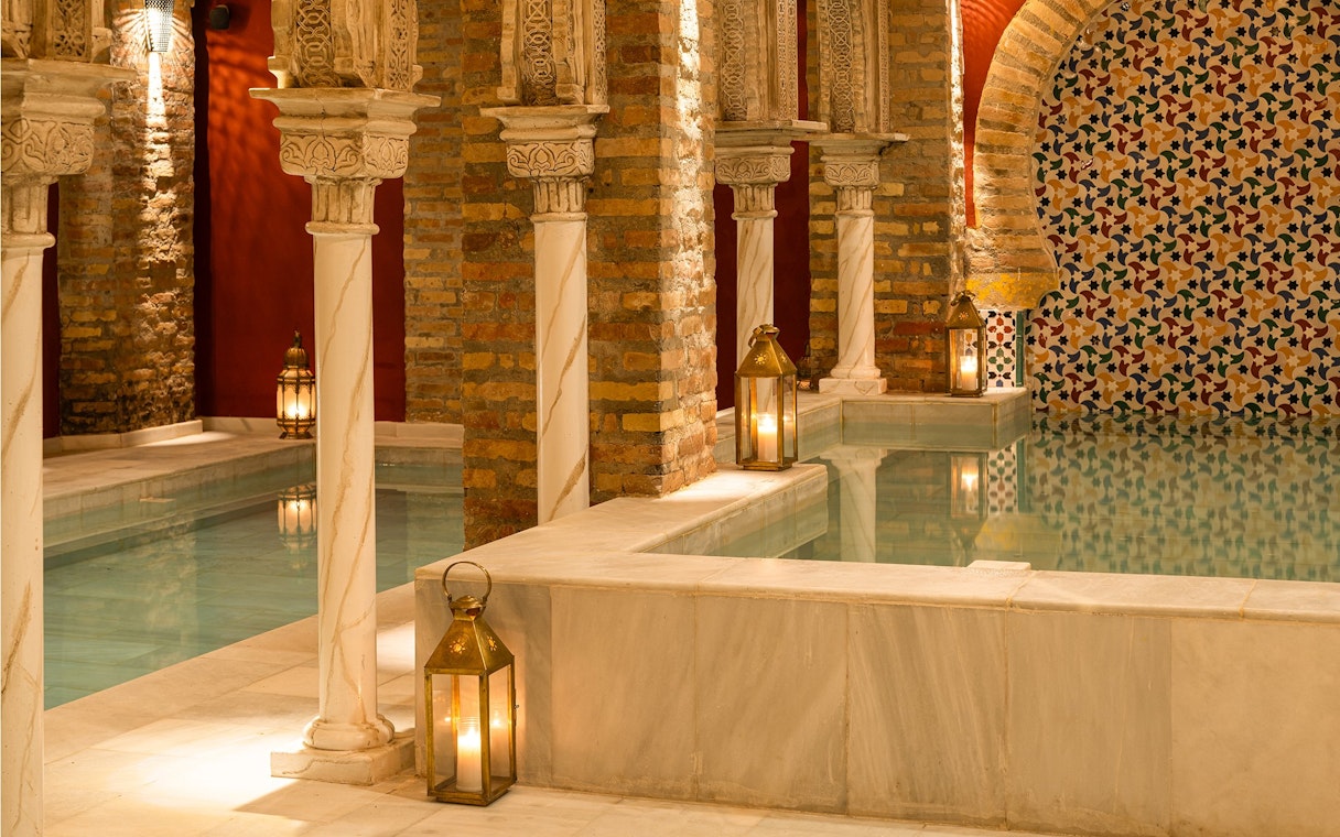 Traditional Hammam Bath interior in Granada with ornate columns and lanterns by the pool.