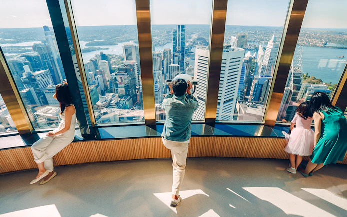 Visitors on Sydney Tower Eye viewing deck overlooking city skyline.