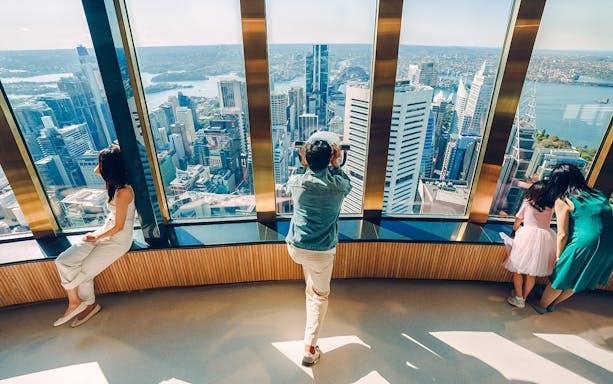 Visitors on Sydney Tower Eye viewing deck overlooking city skyline.