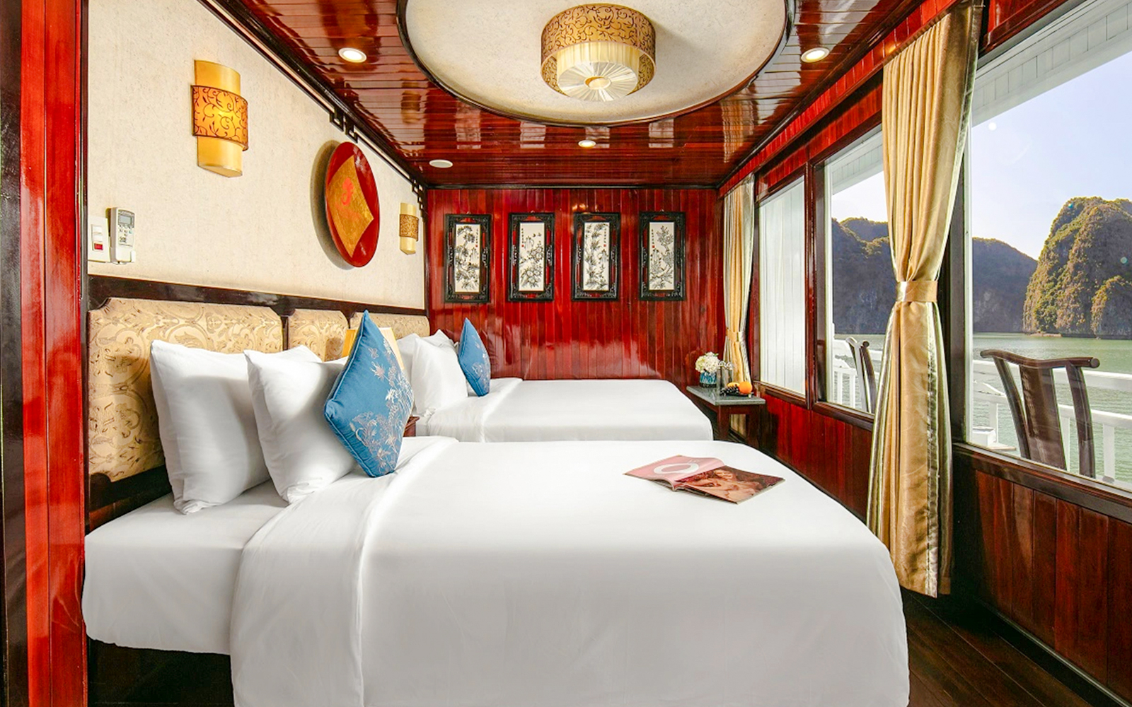 Twin beds in a wood-paneled cabin on a Ha Long Bay cruise ship with karst landscape view.