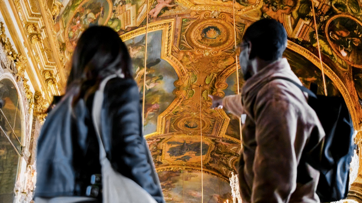 Tourist guided inside Versailles Palace, France, exploring ornate interiors.