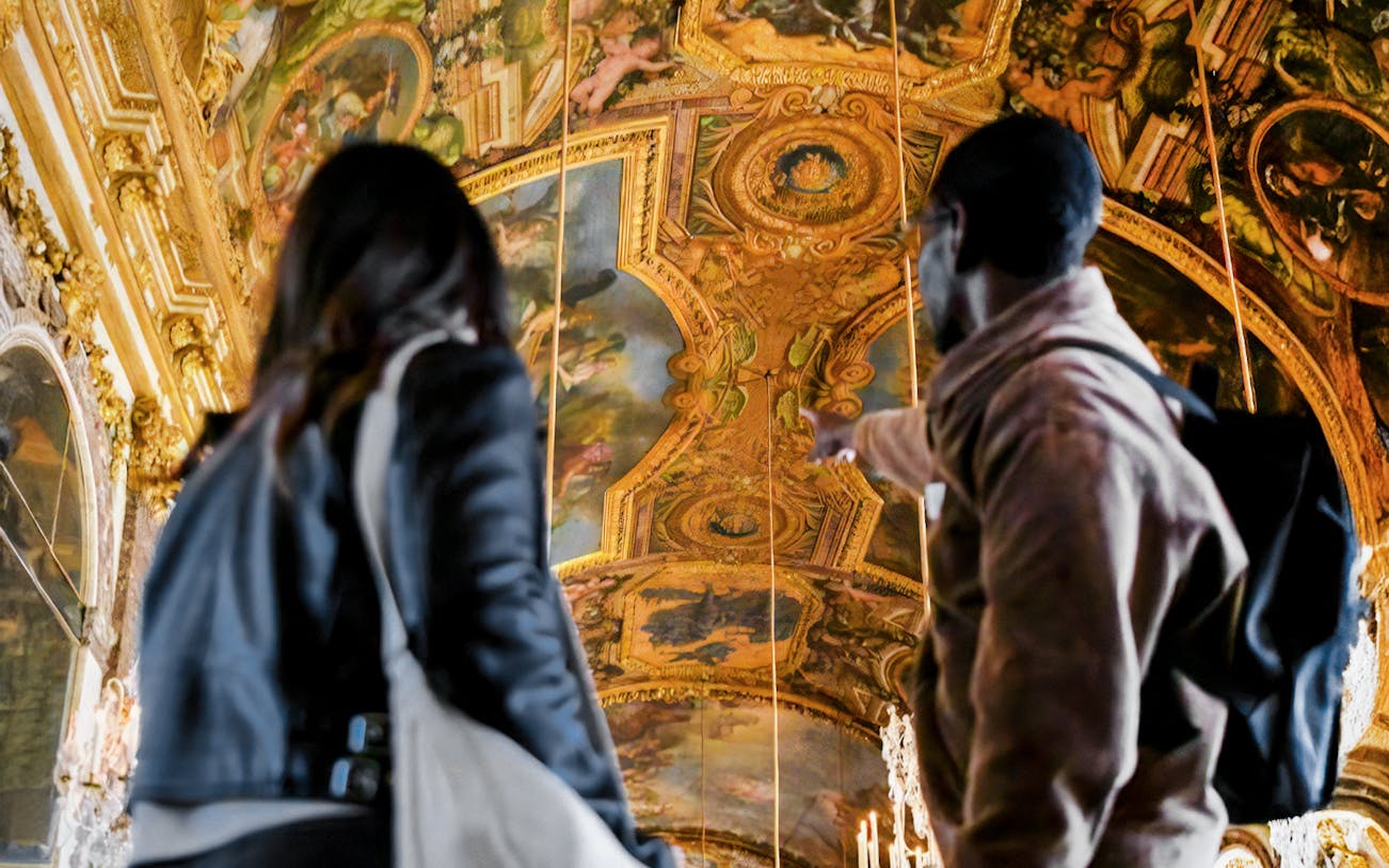 Tourist guided inside Versailles Palace, France, exploring ornate interiors.