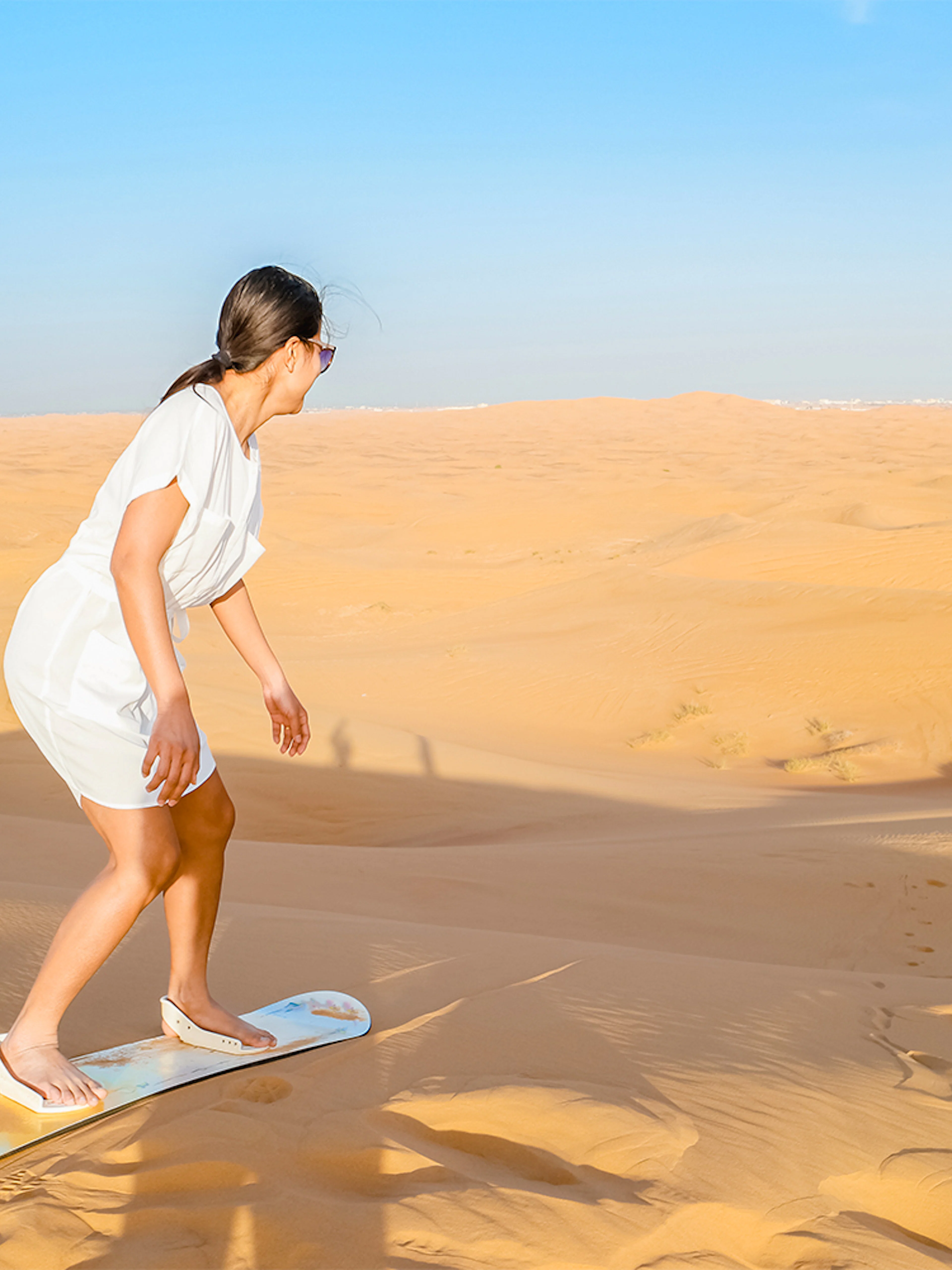Woman sandboarding on a dune in the Dubai desert.