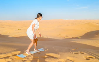 Woman sandboarding on a dune in the Dubai desert.
