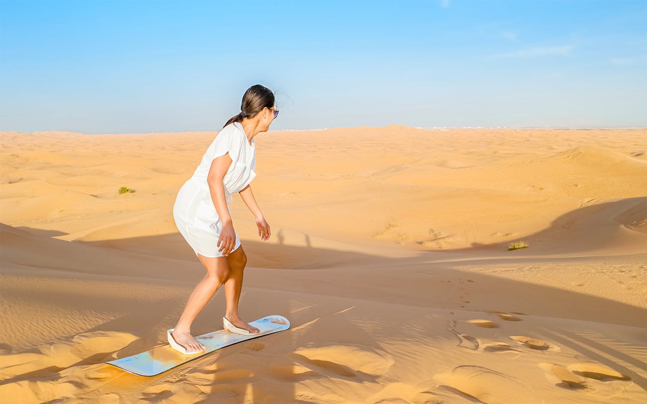 Woman sandboarding on a dune in the Dubai desert.
