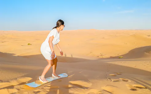 Woman sandboarding on a dune in the Dubai desert.