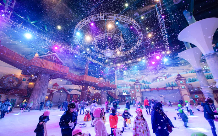 Tourists enjoying indoor winter activities at Vivaldi Park Ski World under colorful lights.