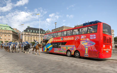Red double-decker bus on a city sightseeing tour in Stockholm, passing a mounted royal guard parade.
