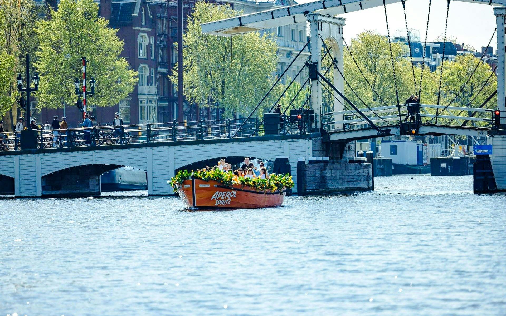 Guests enjoying Aperol Spritz Cruise on Amsterdam canal near historic bridge.