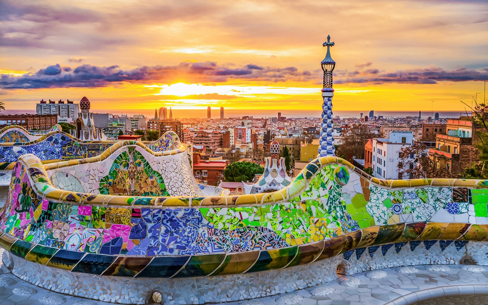 Park Güell's colorful mosaic terrace overlooking Barcelona at sunset.