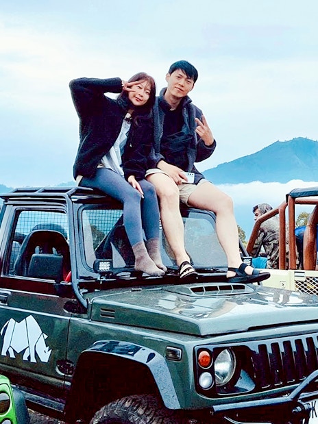 Couple sitting on jeep with Mount Batur in background during Bali sunrise tour.