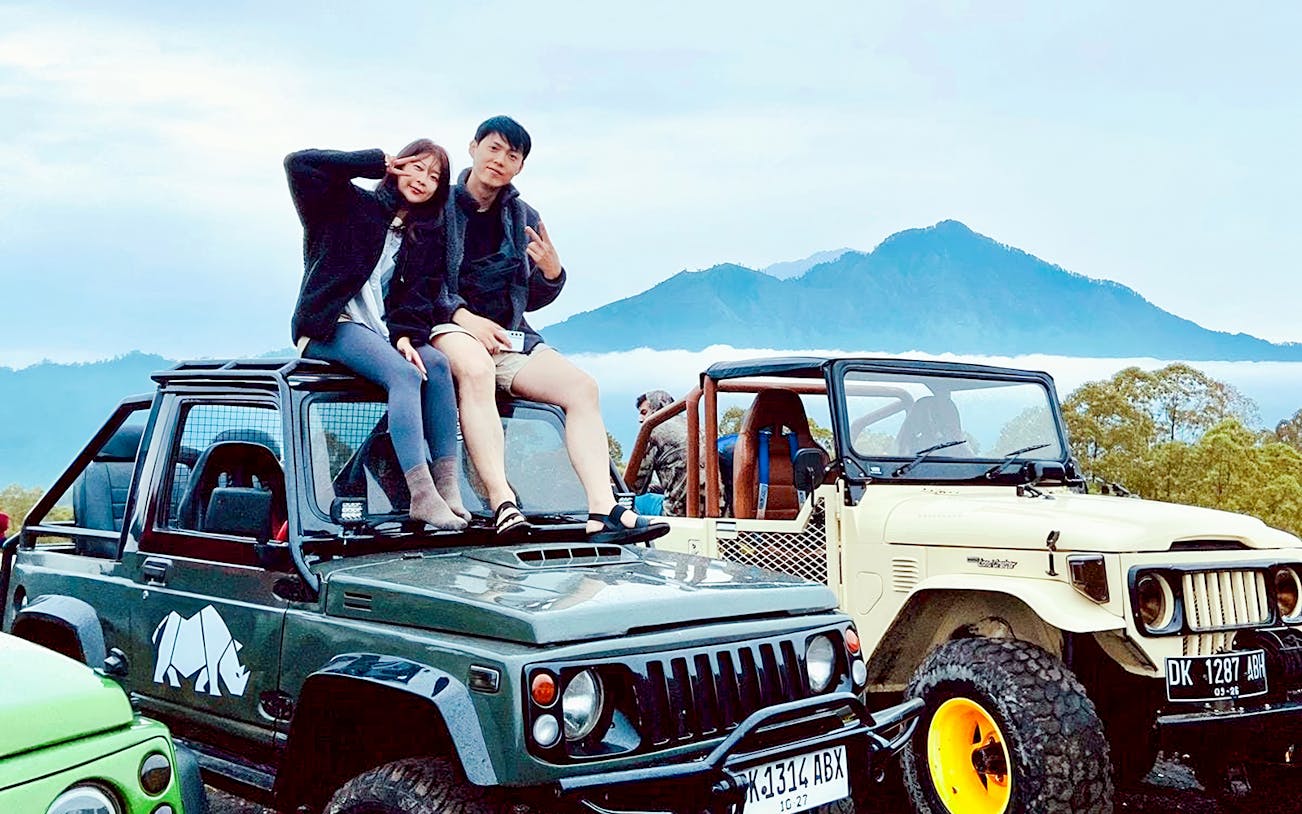Couple sitting on jeep with Mount Batur in background during Bali sunrise tour.