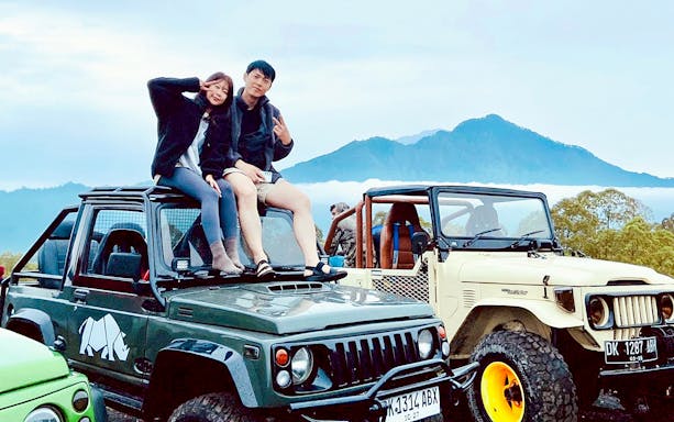 Couple sitting on jeep with Mount Batur in background during Bali sunrise tour.