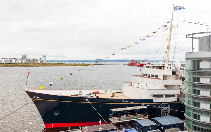 Royal Yacht Britannia docked in Edinburgh with cityscape in the background.