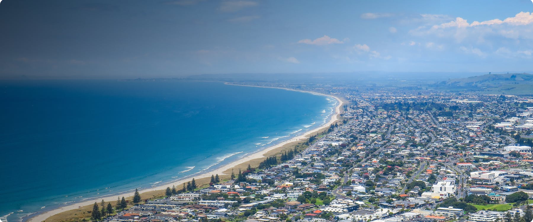Aerial view of Tauranga coastline with cityscape and ocean.