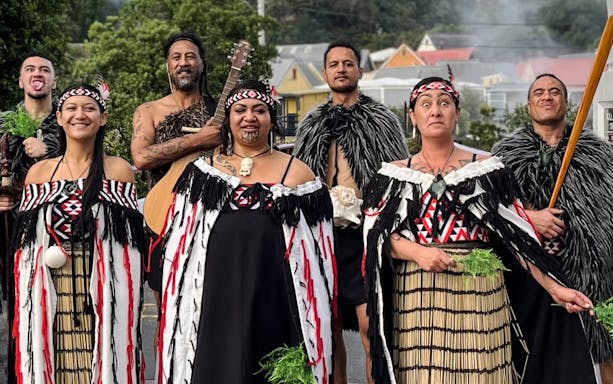 Maori performers in traditional attire with instruments and greenery, New Zealand.