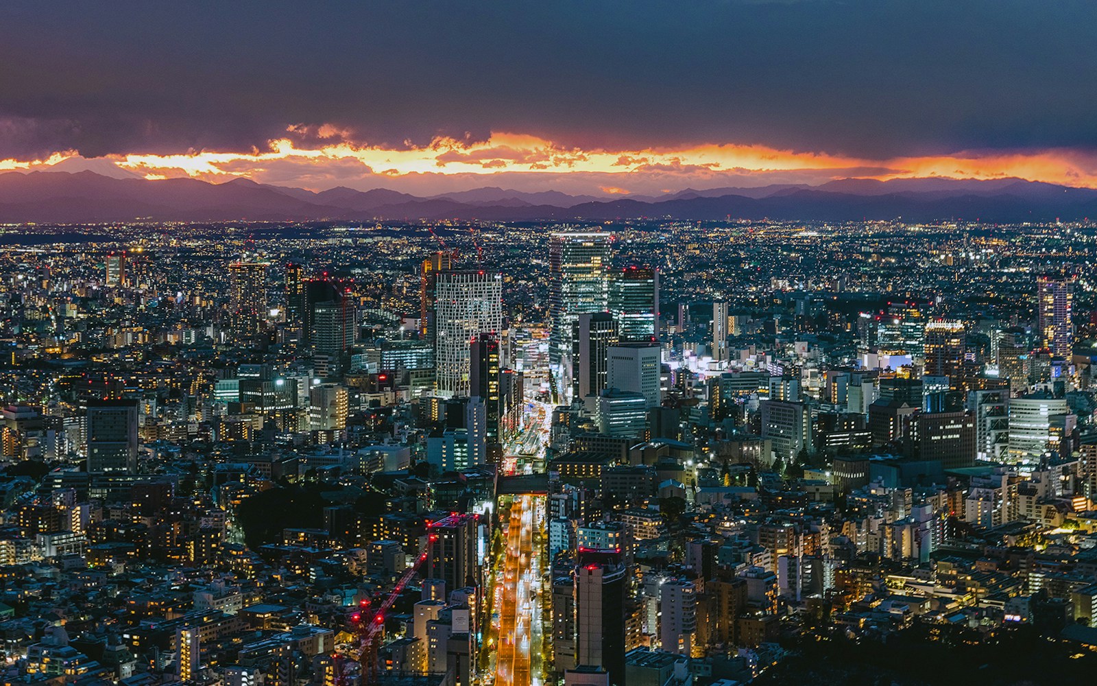 Roppongi Hills skyline at sunset with city lights and distant mountains.