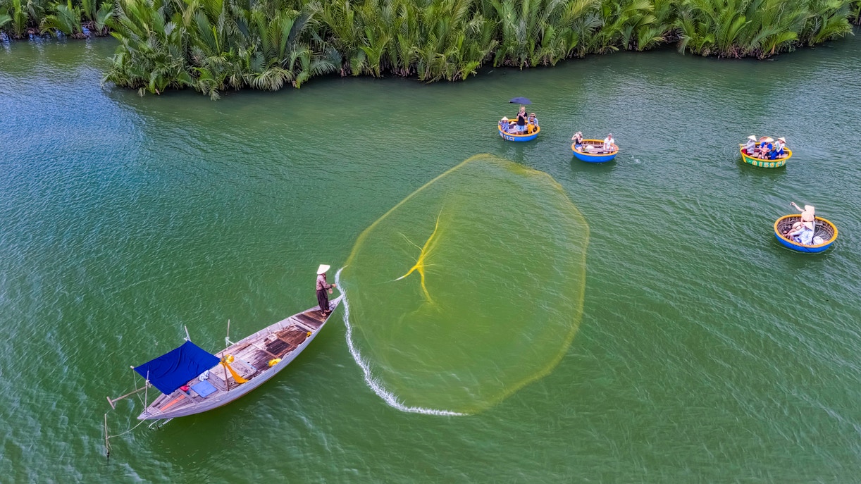 Fisherman casting net from boat near basket boats in coconut water mangrove forest.