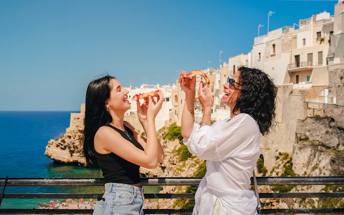 Tourists enjoying pizza with a view of Polignano a Mare during a street food tour.
