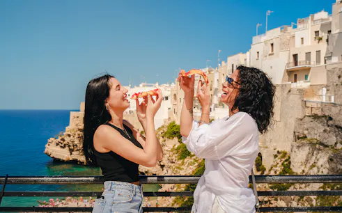 Tourists enjoying pizza with a view of Polignano a Mare during a street food tour.