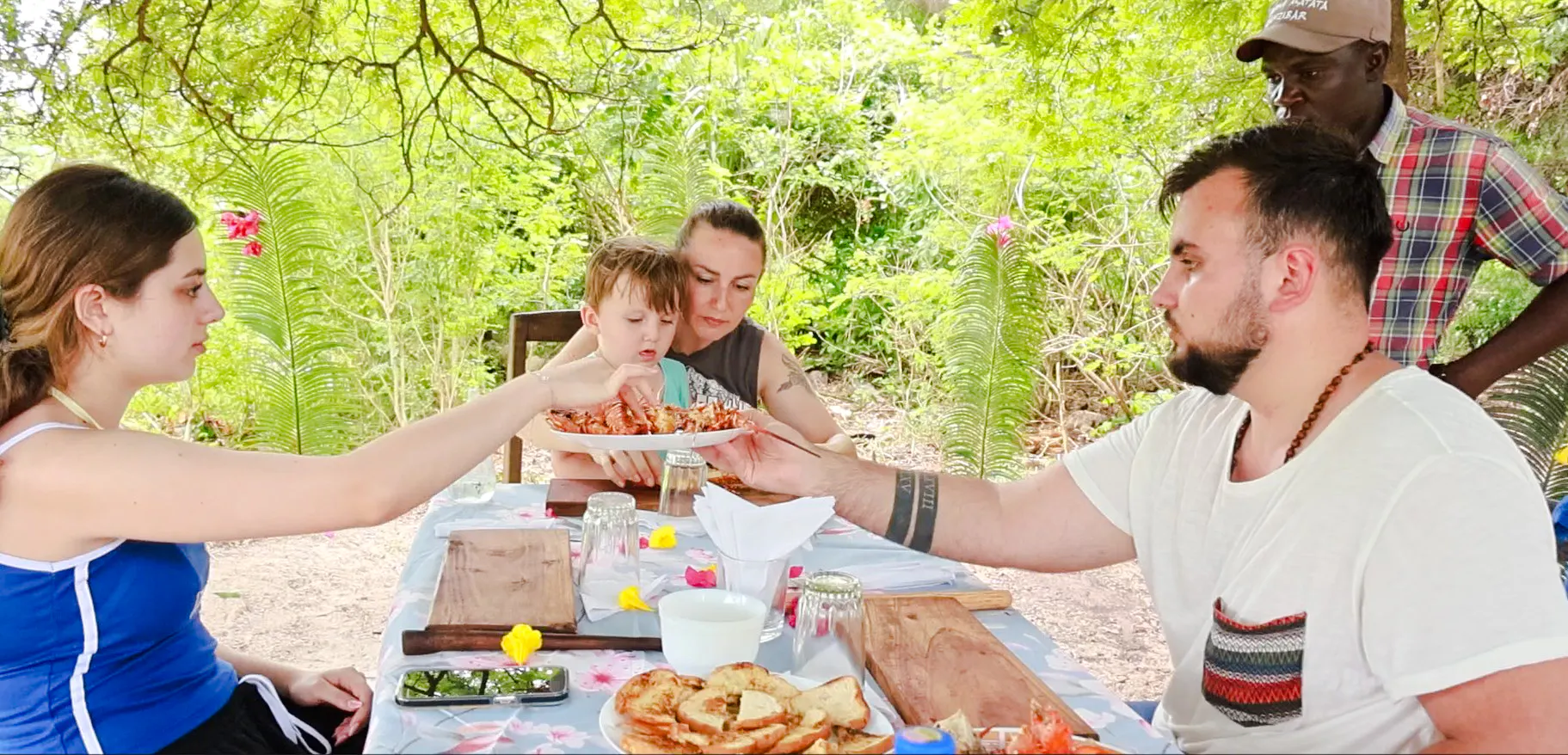 Family enjoying seafood lunch on Funzi Island excursion, surrounded by lush greenery.