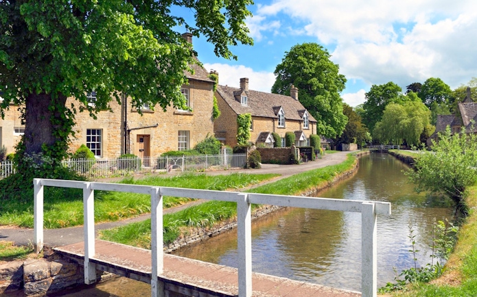 Cotswolds village houses by a canal with a footbridge, part of a small group tour.