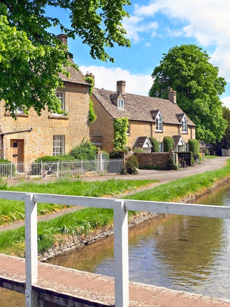 Cotswolds village houses by a canal with a footbridge, part of a small group tour.