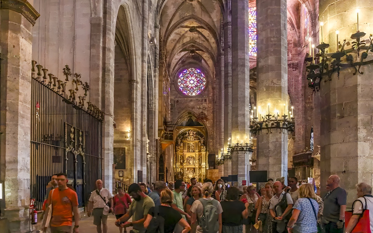 Visitors inside Palma Cathedral exploring Gothic architecture and stained glass windows in Palma, Spain.