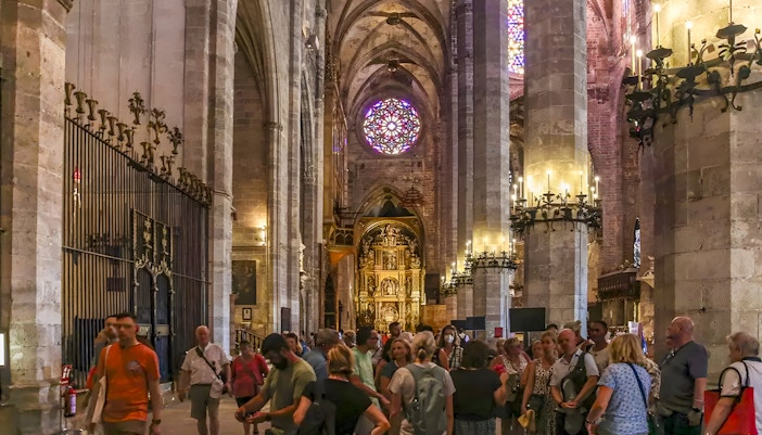 Visitors inside Palma Cathedral admiring Gothic architecture and stained glass windows, Palma, Spain.