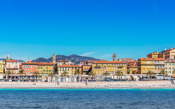 Colorful buildings along Nice's Old Town waterfront, with mountains in the background.