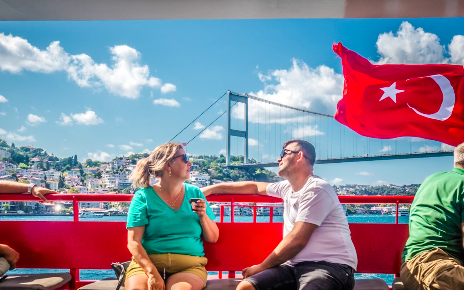 Guests on Bosphorus cruise with Turkish flag and bridge in Istanbul.