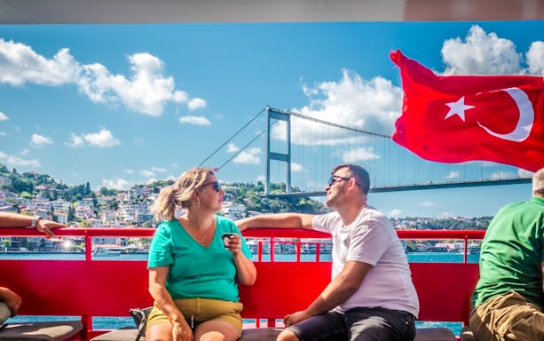 Guests on Bosphorus cruise with Turkish flag and bridge in Istanbul.