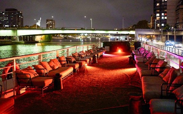 Seine River dinner cruise deck with seating, Paris city lights in background.