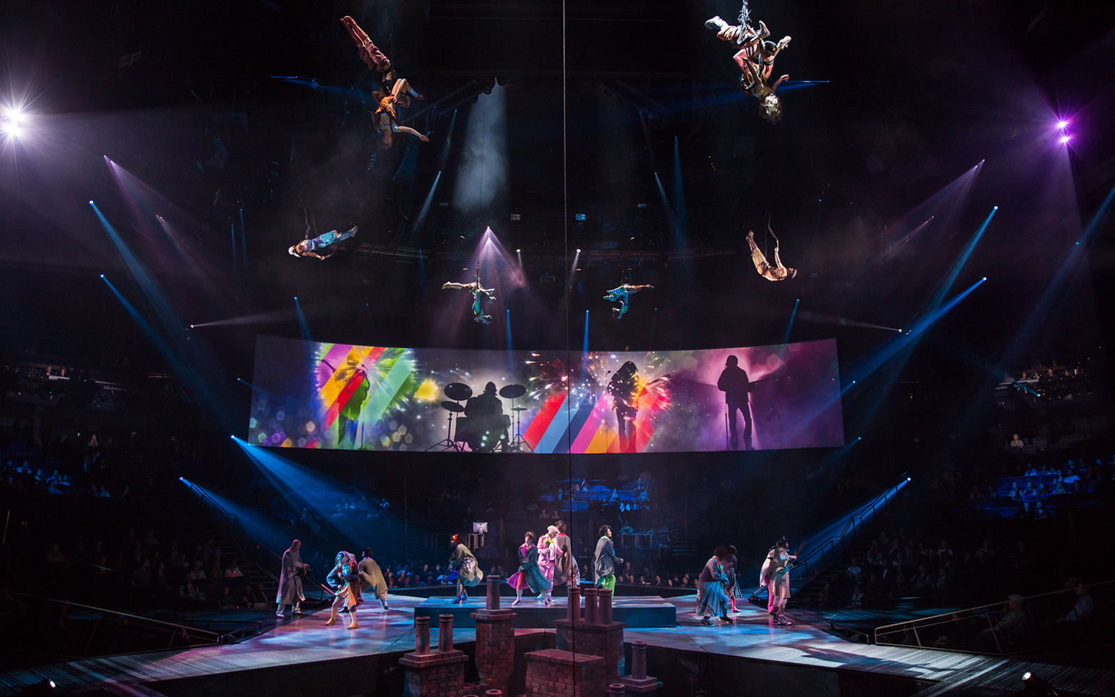 Acrobats performing above stage with colorful Beatles LOVE show backdrop.