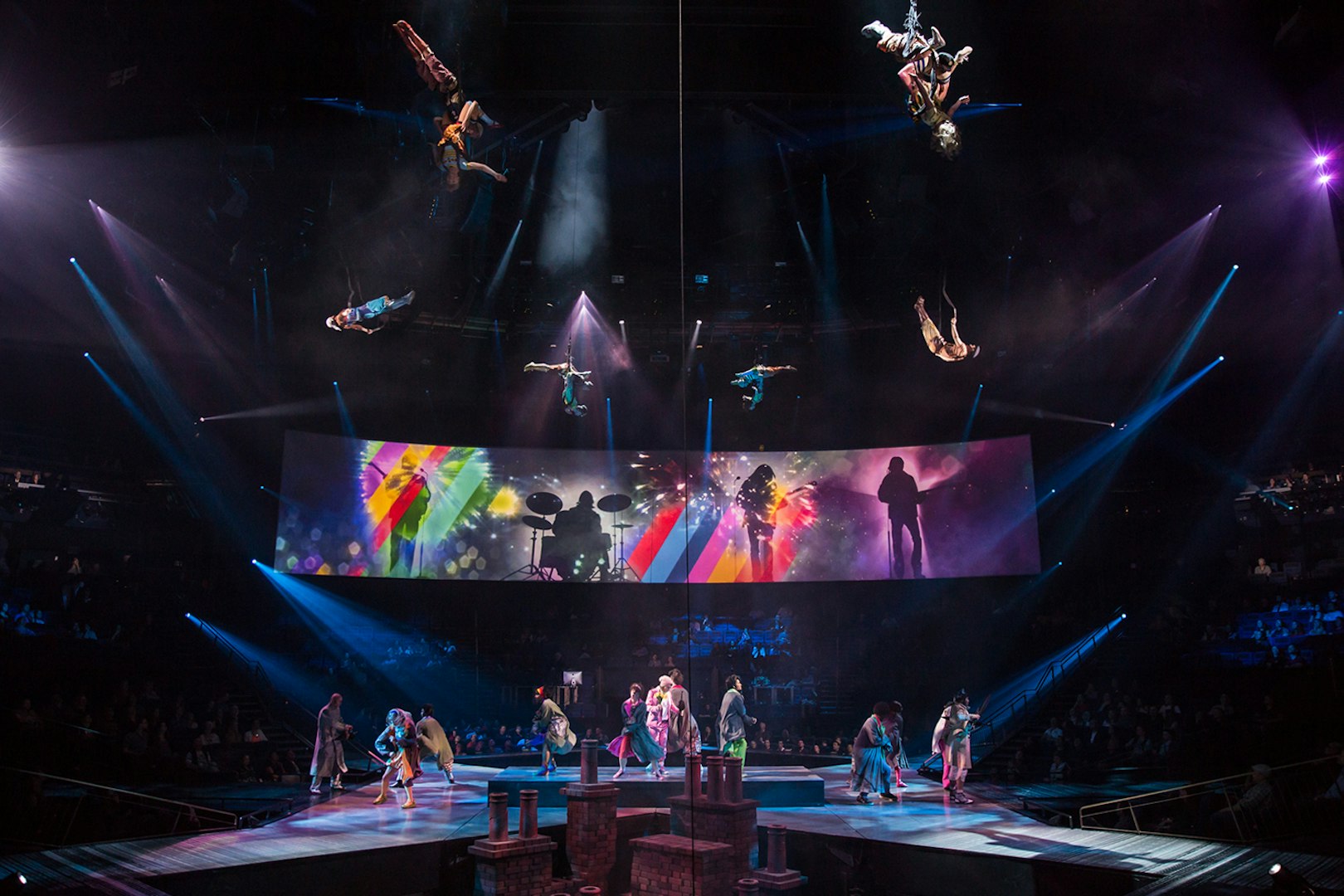 Acrobats performing above stage with colorful Beatles LOVE show backdrop.