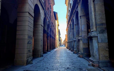 Narrow cobblestone street with historic arches in Bologna, Italy, for a self-guided mystery game.