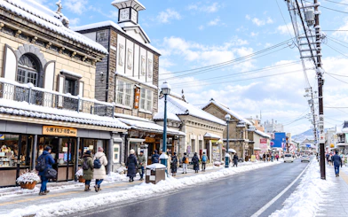 Snow-covered street in Otaru, Hokkaido with people walking past historic buildings.