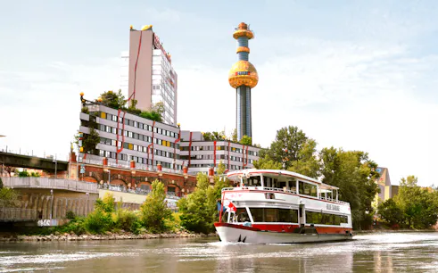 MS Blue Danube cruise on Danube Canal, Vienna, with Spittelau incineration plant in background.