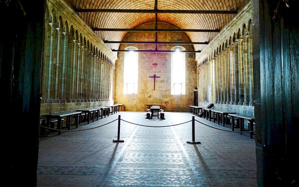 Mont-Saint-Michel Abbey interior with stone columns and wooden benches.