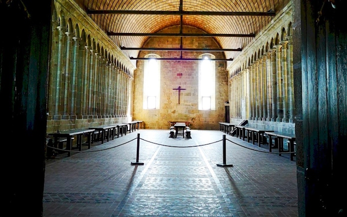 Mont-Saint-Michel Abbey interior with stone columns and wooden benches.