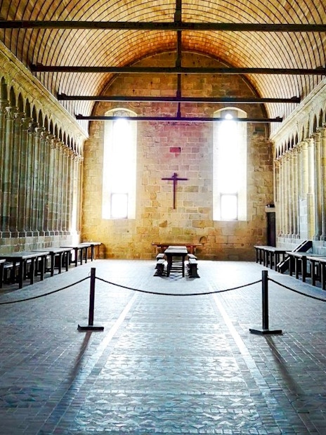 Mont-Saint-Michel Abbey interior with stone columns and wooden benches.