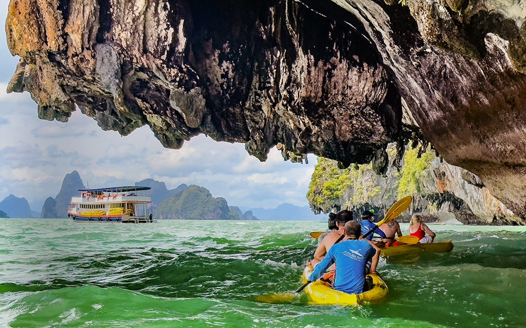 Kayakers exploring islands under limestone cliffs with a tour boat in the background.