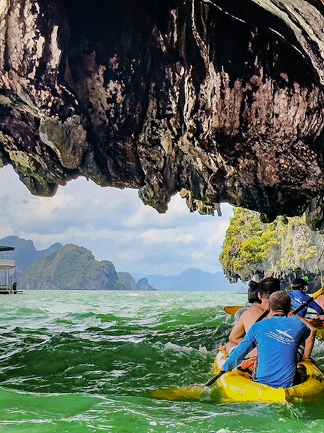 Kayakers exploring islands under limestone cliffs with a tour boat in the background.