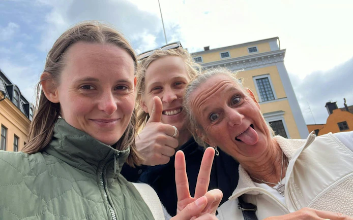 Three people smiling and posing in front of historic buildings in Stockholm.