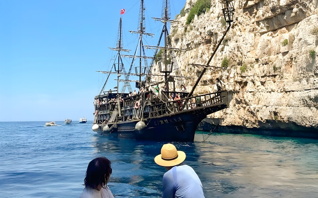 Pirate ship on Vlora's Ionian Odyssey tour, Albania, near rocky coastline.