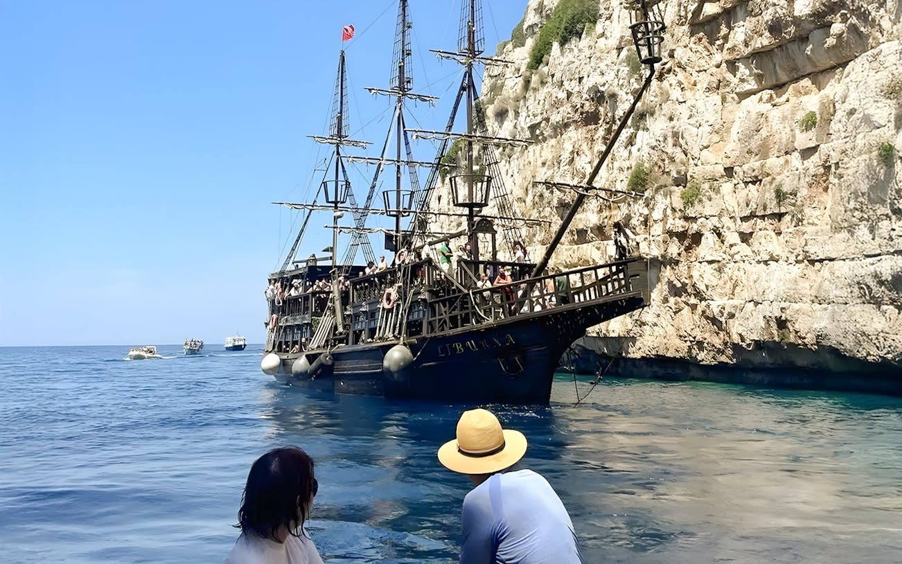 Pirate ship on Vlora's Ionian Odyssey tour, Albania, near rocky coastline.