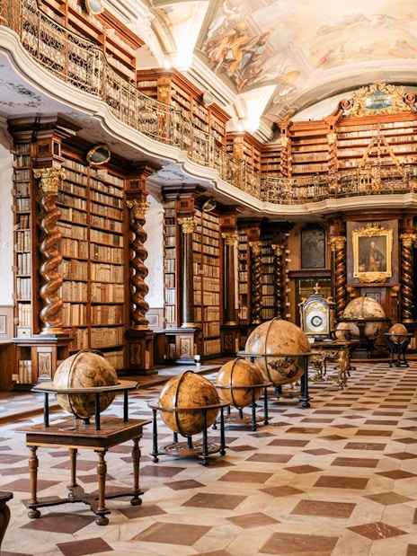 Prague Klementinum Library interior with ornate bookshelves and globes.